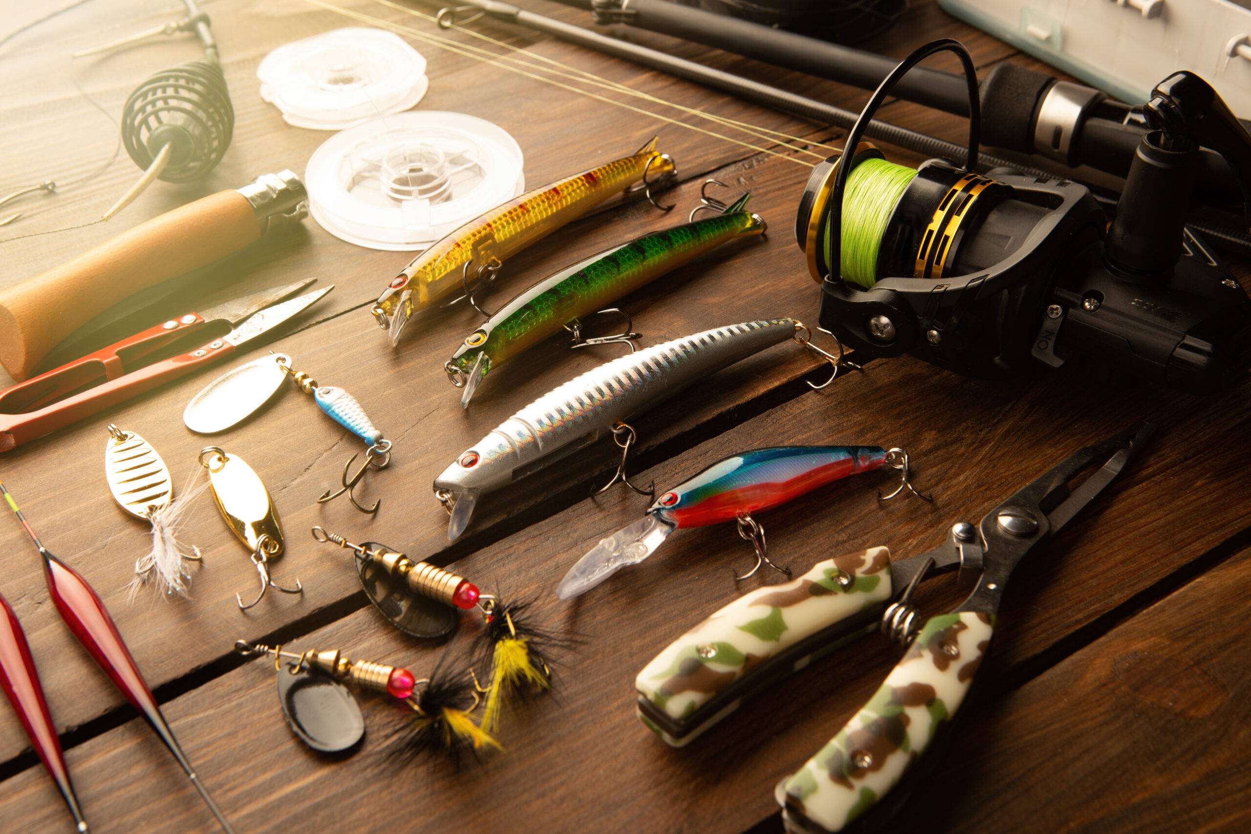 Fishing lures, spinners, spoons and a spinning reel laid out on a wooden table