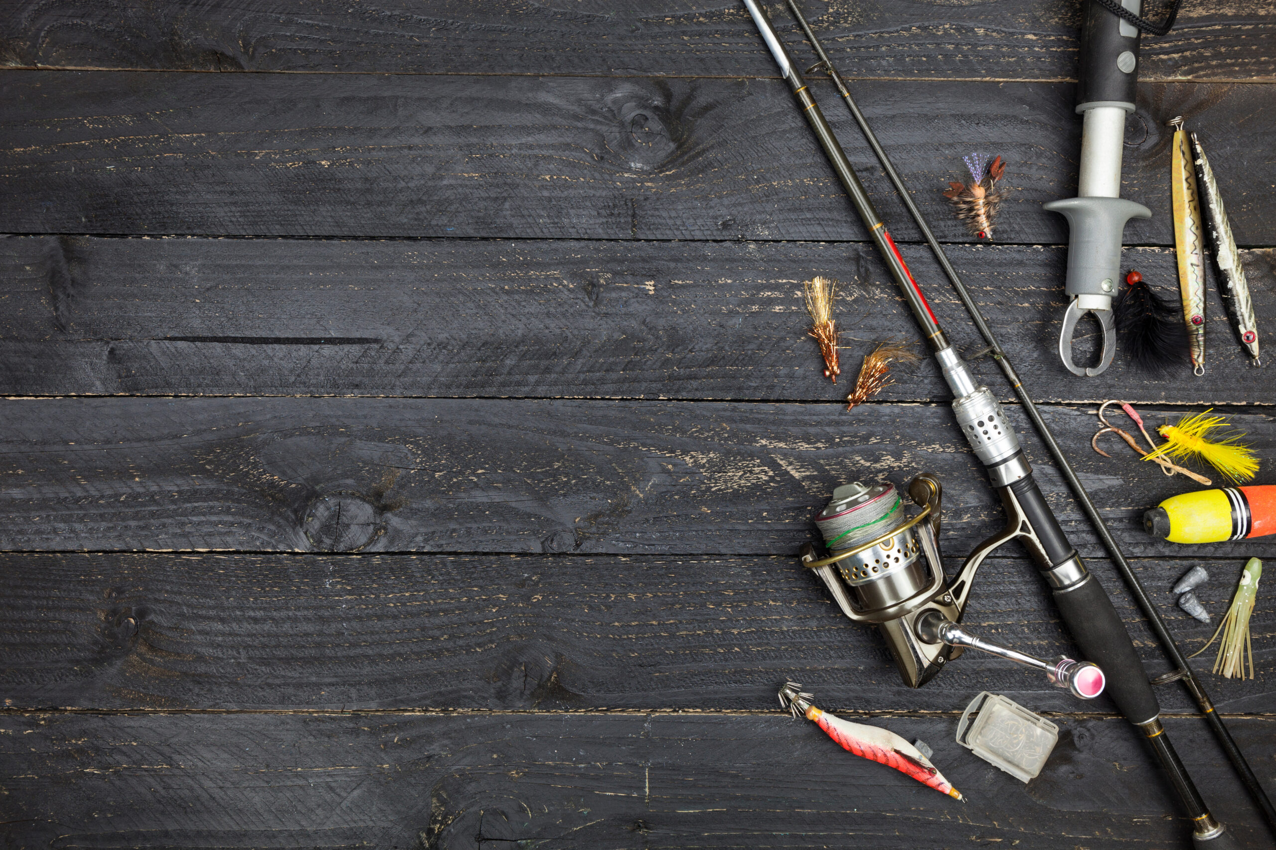 Spinning rod and reel with lures and fishing tackle on dark wooden boards